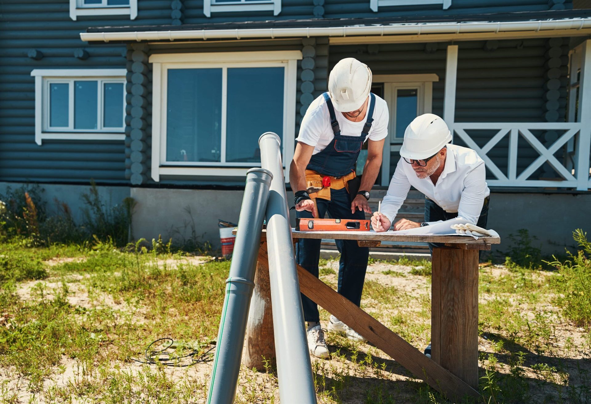 Two construction workers reviewing building plans outside a residential property