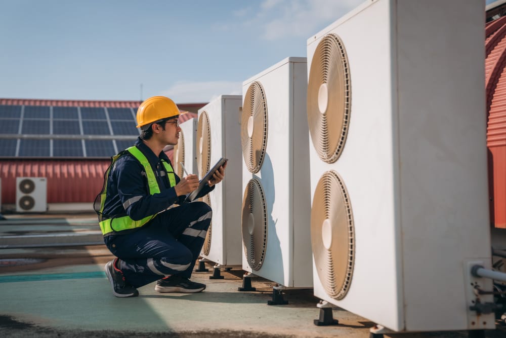 Technician in safety gear inspecting rooftop air conditioning units for maintenance and repairs.