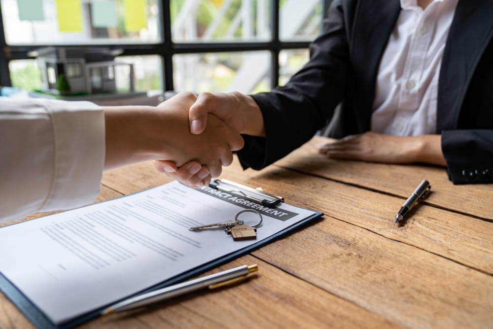 Two professionals shaking hands over a signed agreement with house keys on the table, symbolizing property management services and agreements.