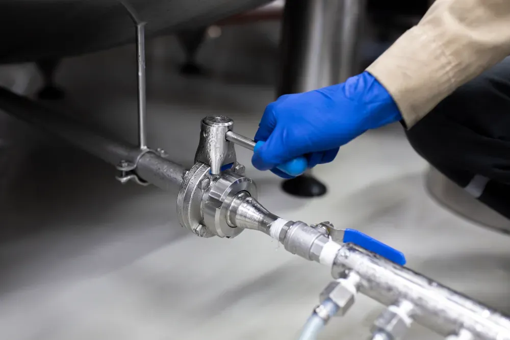 Professional plumber adjusting a stainless steel pipe valve, wearing protective gloves for safety